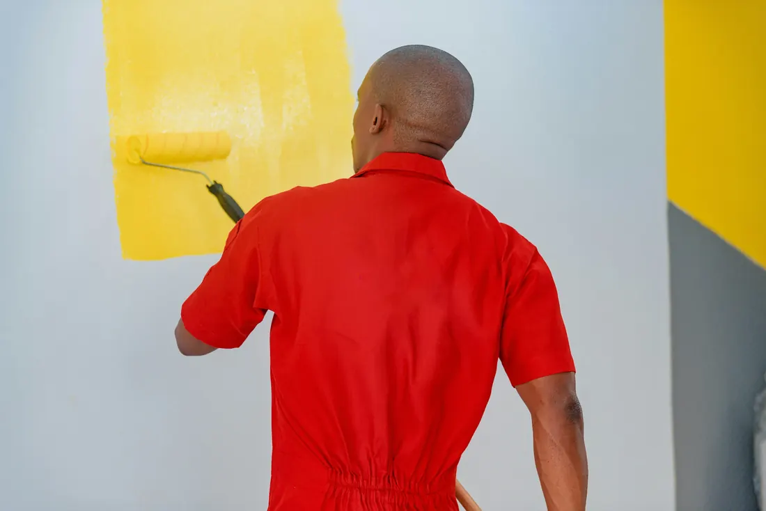 Maler im roten Überkleid rollt gelbe Farbe auf eine Wand